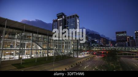 Kapstadt, Südafrika - 24. Dezember 2025: Blick auf die moderne Glasfassade des CTICC, die die Lichter der Stadt vor dem Hintergrund des Tafelbergs reflektiert Stockfoto