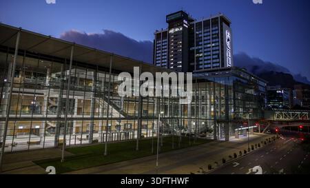 Kapstadt, Südafrika - 24. Dezember 2025: Blick auf die moderne Glasfassade des CTICC, die den Dämmerhimmel reflektiert, mit dem Tafelberg in weichem, e Stockfoto