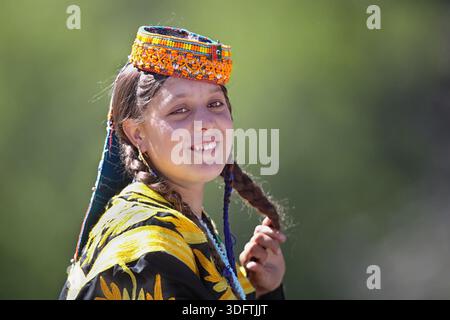 Kalash, Pakistan - 24. Dezember 2025: Blick auf eine Kalashi-Frau in traditioneller Kleidung, ihren lebendigen Kopfschmuck und ihren gestickten Schal in starkem Kontrast zu Agave Stockfoto