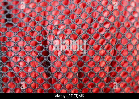 Nahaufnahme-Textur aus lebendigem rotem Synthetik-Gewebe unter dunkelgrauer Netzschicht mit Musterdetails aus Textil mit Wabenstruktur, das für Sportbekleidung verwendet wird m Stockfoto
