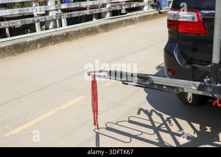 Leerer hinterer Fahrradträger aus Metall am schwarzen Stoßfänger des suv-Autos mit rotem Riemen, der bereit für ein Abenteuer auf einer Betonbrücke mit fröhlichem Urlaub ist Stockfoto