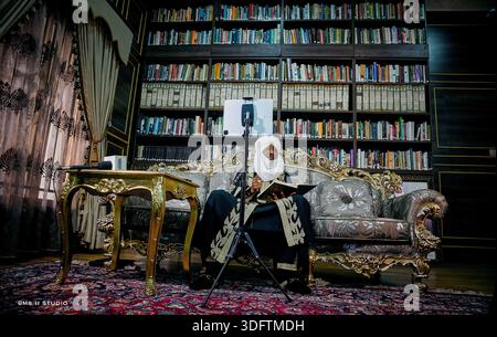 Kano City, Nigeria - 20. Januar 2021: Blick auf einen Mann in traditioneller Kleidung, der vor dem Hintergrund von raumhohen Bücherregalen ein Buch liest. Stockfoto