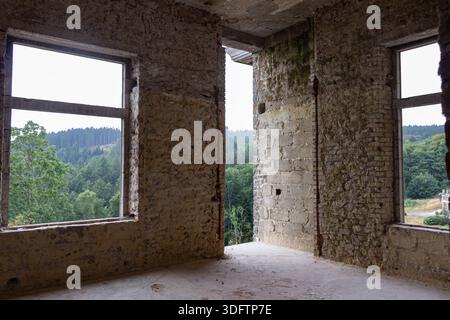 Blick durch ein großes Loch oder ein abgerissenes Fenster auf die Waldlandschaft. Sie stehen in einem leeren und verlassenen Gebäude mit abgestreiften Wänden. Stockfoto