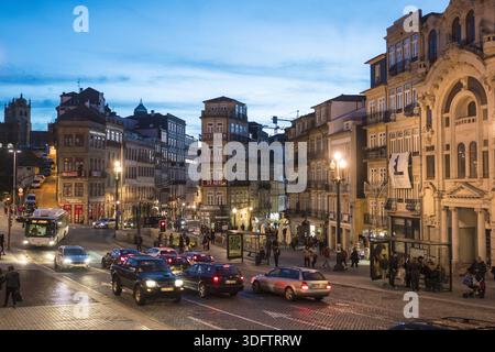 Porto, Portugal - 26. November 2017: Blick auf die belebte Stadtstraße leuchtet mit warmem Licht vor dem kühlen Dämmerhimmel, eingerahmt vom kunstvollen Archit Stockfoto