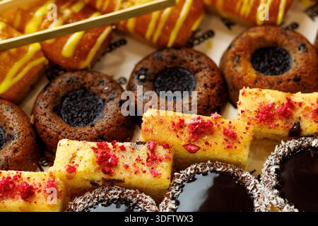 Nahaufnahme mit verschiedenen Mini-Kuchen und Gebäck mit Schokolade, Beeren und Kokosnuss auf einem gefütterten Serviertablett. Bunte Dessert-Auswahl für Catering, teilweise Stockfoto