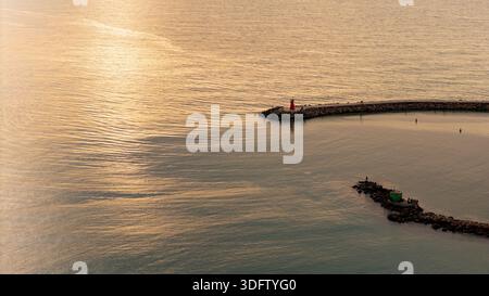 Drohnenblick auf die Morgensonne, die hinter Wolken über einer ruhigen Meeresbucht aufgeht Stockfoto