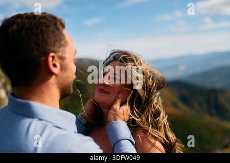 Mann, der das Gesicht der Frauen in einer romantischen Geste gegen eine Berglandschaft hält Stockfoto