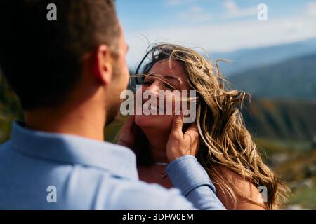 Mann, der das Gesicht der Frauen in einer romantischen Geste gegen eine Berglandschaft hält Stockfoto