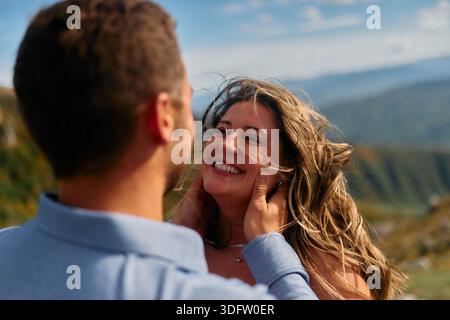 Mann, der das Gesicht der Frauen in einer romantischen Geste gegen eine Berglandschaft hält Stockfoto