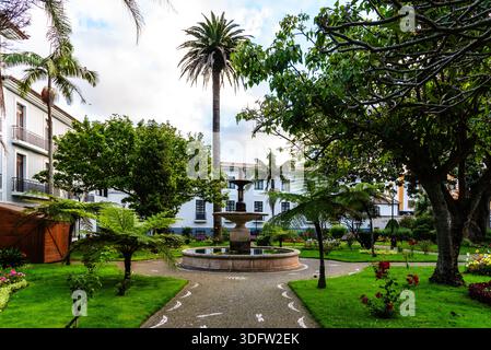Ein wunderschöner Park in Angra do Heroismo, Terceira, Azoren, mit einem Brunnen, üppigem Grün, und Palmen unter bewölktem Himmel. Stockfoto