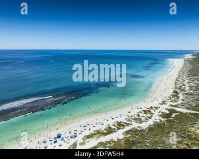 Aus der Vogelperspektive auf das türkisfarbene Meer, das sanft den unberührten weißen Sand küsst, wo sich winzige Figuren unter dem klaren blauen Himmel, Yanchep, Wester, sonnen Stockfoto
