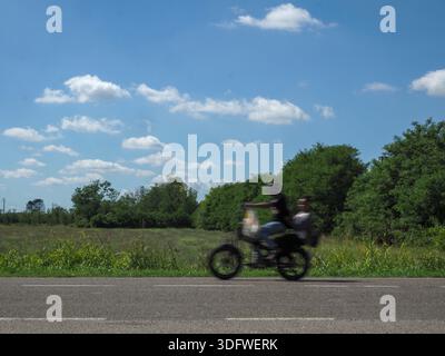 Ein Paar genießt eine aufregende Motorradfahrt durch eine wunderschöne grüne Landschaft an einem sonnigen Tag. Stockfoto