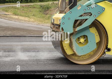 Neue Asphaltstraße. Die gelbe Straßenwalze, die auf der neuen Straße mit Rauch arbeitet Stockfoto