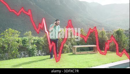 Sprechender asiatischer Mann, der hellgrünes Polo auf dem Rasen am Pool trägt, Smartphone hält, rotes Diagramm überlagert Stockfoto