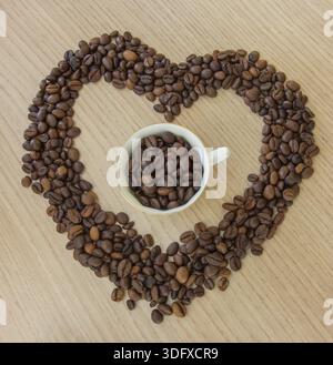 Morgenherz. Herzform aus Kaffeebohnen und einer Tasse Kaffee in der Mitte Stockfoto