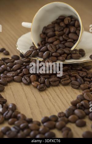 Morgenherz. Herzform aus Kaffeebohnen und einer Tasse Kaffee mit Bohnen, verschwommen Stockfoto