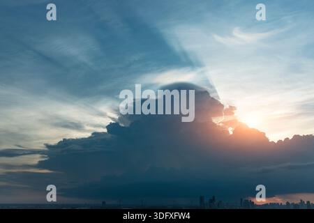 Ein atemberaubender Sonnenuntergang wirft Licht durch dunkle Wolken über der Skyline der Stadt. Die Strahlen bilden einen schönen Kontrast zu den Blau- und Grautönen am Himmel Stockfoto