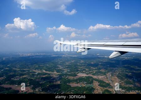 Flugzeugflügel, Bullauge, Blick von Flugzeug zu Flügel. Das Flugzeug fliegt über eine Stadt mit einem grünen Feld darunter Stockfoto