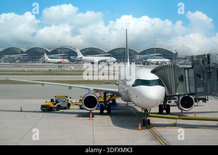 Das Passagierflugzeug parkt auf dem Rollfeld am Hong Kong International Airport. Eine Bordbrücke verbindet das Flugzeug. Das Flughafenpersonal arbeitet in der Nähe an der Stockfoto