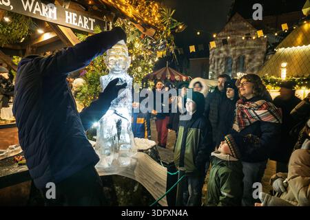 Besucher sehen zu, wie Männer eine Eisskulptur auf dem Rigaer Weihnachtsmarkt erschaffen Stockfoto