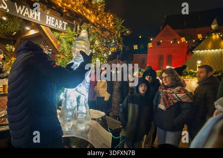 Besucher sehen zu, wie Männer eine Eisskulptur auf dem Rigaer Weihnachtsmarkt erschaffen Stockfoto
