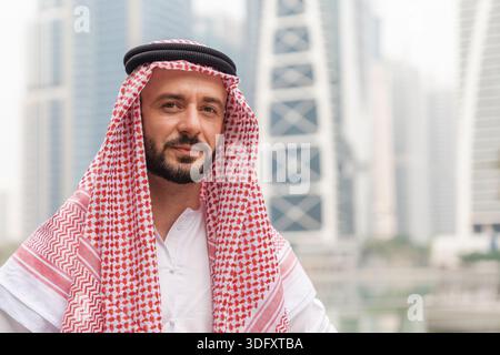 Arabischer Geschäftsmann in traditioneller nahöstlicher Kleidung steht im Stadtgebiet. Er zeigt Vertrauen und Professionalität im Finanzviertel. Stockfoto