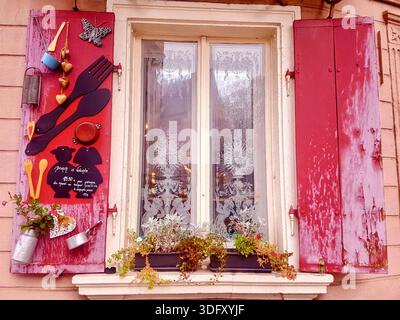Typisch elsässisches Fenster mit roten Fensterläden, dekoriert mit farbenfrohen traditionellen Details. Ein charmantes architektonisches Element, das das Elsass widerspiegelt. Stockfoto