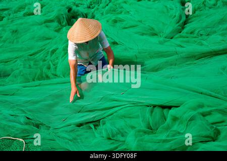 Mann Guy in traditionellem authentischem Hut vietnamesisches Entwirren grüner Fischernetze, die sich auf das Angeln vorbereiten und auf das Meer gehen. Stockfoto