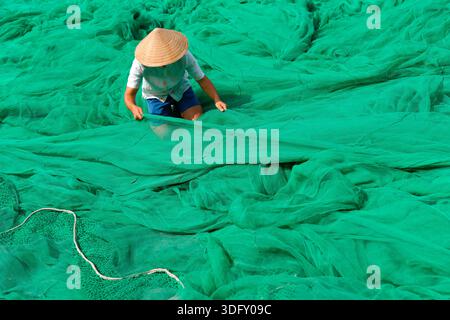 Mann Guy in traditionellem authentischem Hut vietnamesisches Entwirren grüner Fischernetze, die sich auf das Angeln vorbereiten und auf das Meer gehen. Stockfoto