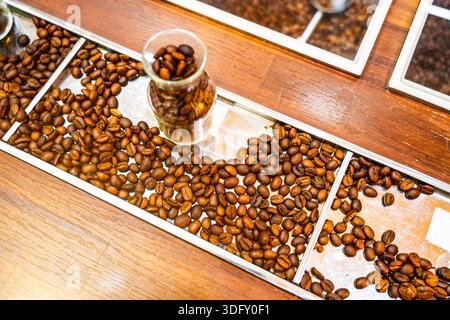 Verschüttete geröstete Kaffeebohnen in Glasbechern auf der Theke. Stockfoto