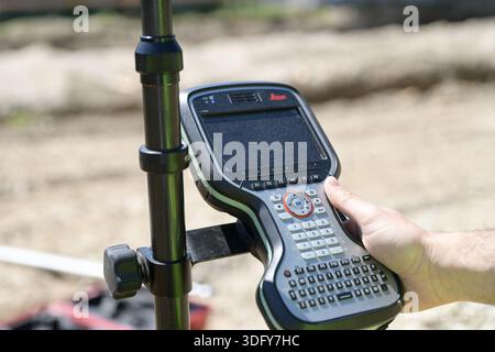 Ein Vermesser, der einen tragbaren Datencontroller von Leica Geosystems während der Landmessung auf einer Baustelle hält Stockfoto