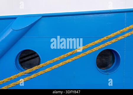 Ein dickes Anlegeseil ist am Bug eines blau-weißen Bootes befestigt. An der Seite des Bootes sind zwei kreisförmige Fenster zu sehen Stockfoto