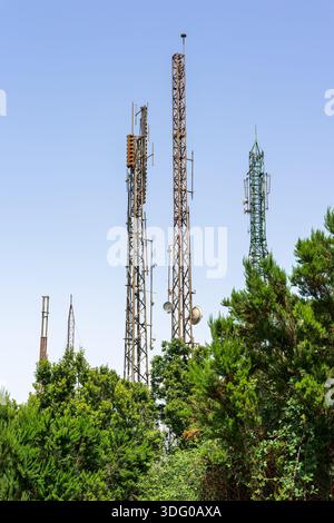 Handymasten mit Antennen über grünen Bäumen, Telekommunikationsinfrastruktur vor klarem blauem Himmel. Stockfoto