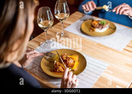 Zwei Personen sitzen an einem Holztisch mit Gläsern Wein. Sie essen zu Abend, mit Tellern mit Essen vor ihnen. Die Atmosphäre ist warm und einladend Stockfoto
