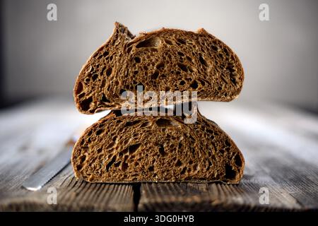 Zwei frische Hälfte Roggensauerteig Brot in Sektion auf einem rustikalen Holzbrett. Handwerklicher Bauernbrot in warmem natürlichem Licht Stockfoto