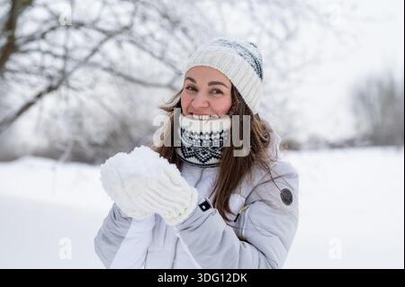 Fröhliche Frau in warmen Winterkleidung, die in einem verschneiten Park steht und die Winteratmosphäre genießt Stockfoto
