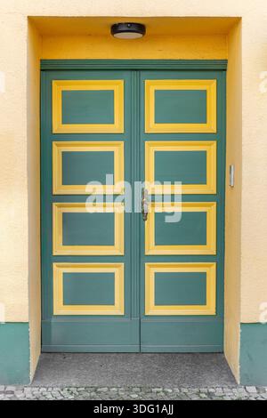Grüne Tür mit gelben Paneelen an sonniger Fassade. Heller geometrischer Eingang. Stockfoto