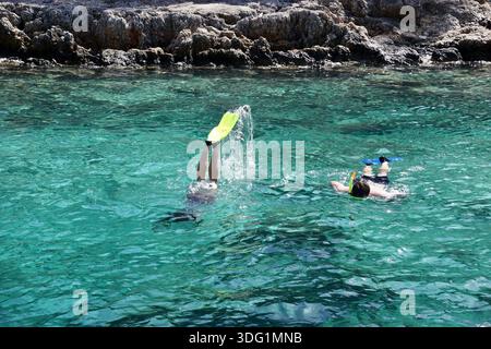 Menschen schwimmen und schnorcheln in klaren türkisfarbenen Küstengewässern in der Türkei in der Nähe einer felsigen Küste und genießen an einem Sommertag ruhige Meeresbedingungen. Stockfoto