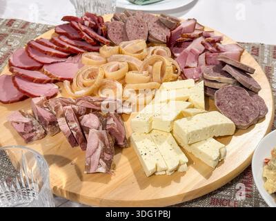 Ein Holzbrett zeigt eine Auswahl an Aufschnitt, Käse und Zwiebelringen und bietet eine rustikale und appetitliche Präsentation perfekt für Versammlungen Stockfoto