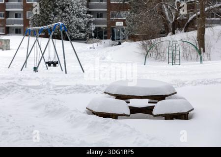 Schneebedeckter Picknicktisch in einem Wohnpark mit Spielplatz im Winter Stockfoto