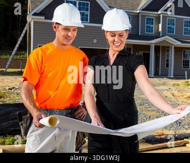 Auf einer sonnendurchfluteten Baustelle studieren ein Bauarbeiter und ein Ingenieur gemeinsam Blaupausen, messen Linien und besprechen Details, während sich der Rahmen erhöht, Team Stockfoto