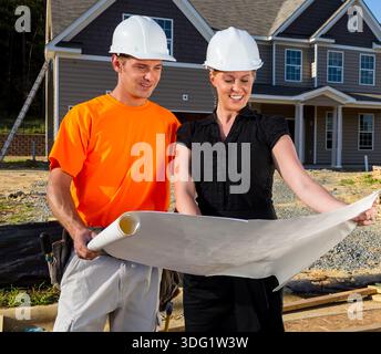 Auf einer sonnendurchfluteten Baustelle studieren ein Bauarbeiter und ein Ingenieur gemeinsam Blaupausen, messen Linien und besprechen Details, während sich der Rahmen erhöht, Team Stockfoto