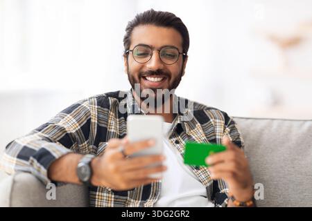 Fröhlicher arabischer Mann mit Kreditkarte und Handy Stockfoto