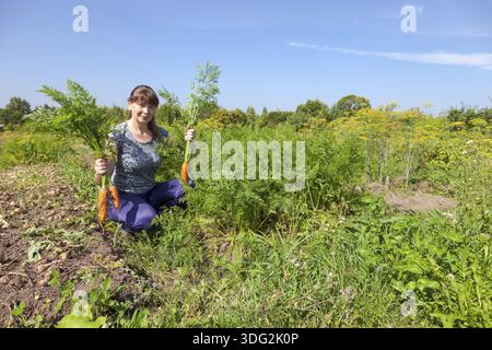Junge Frau, die eine Garbe von Karotten in der Hand halten Stockfoto