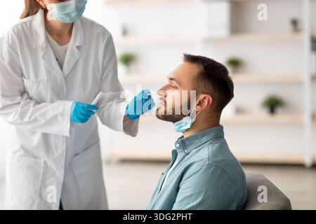 Covid-Diagnoseverfahren. Arzt, der nasalen PCR-Test für jungen kaukasischen Mann mit sterilen Abstrichstäbchen zu Hause macht Stockfoto