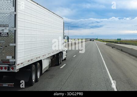 Ein Lkw-Fahrer fährt einen großen Lkw auf einer Autobahn in Elverta, Kalifornien. Der Lkw nähert sich offenen Feldern unter blauem Himmel. Stockfoto