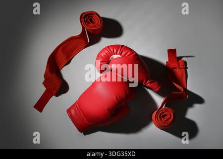 Rote Boxhandschuhe mit Armbändern auf grauem Hintergrund Stockfoto