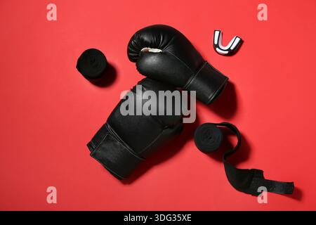 Ein Paar schwarze Boxhandschuhe mit Armbändern und Mundstück auf rotem Hintergrund Stockfoto