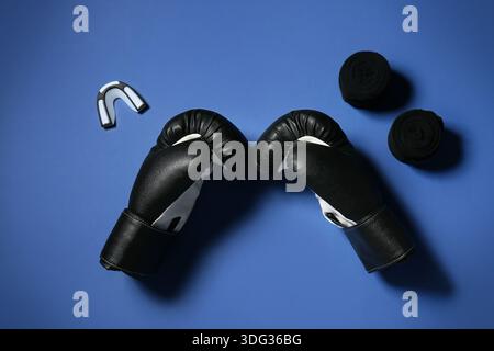 Ein Paar schwarze Boxhandschuhe mit Armbändern und Mundstück auf blauem Hintergrund Stockfoto