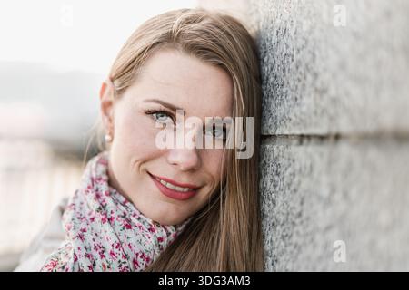 Lächelnde junge Frau draußen an der Wand Stockfoto
